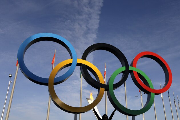 A spectator poses for a photo under the Olympic Rings at the 2014 Winter Olympics, Wednesday, Feb. 12, 2014, in Sochi, Russia. The Winter Olympics are in full swing, but warm temperatures in the Black Sea resort town of Sochi made heavy coats and scarves unnecessary on Wednesday. (AP Photo/Mark Baker)