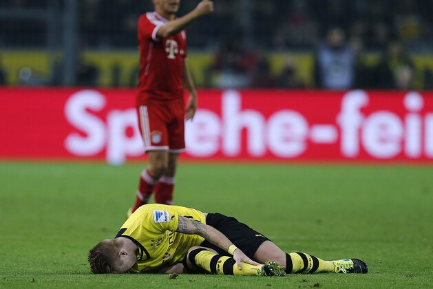 Dortmund's Marco Reus lies injured on the pitch as Bayern's Rafinha, rear, points  during the German first division Bundesliga soccer match between BvB Borussia Dortmund  and Bayern Munich in Dortmund, Germany, Saturday, Nov. 23, 2013. (AP Photo/Frank Augstein)