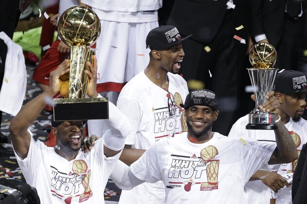 The Miami Heat's Dwyane Wade, left, holds the Larry O'Brien NBA Championship Trophy as  LeBron James holds his Bill Russell NBA Finals Most Valuable Player Award after Game 7 of the NBA basketball championship against the San Antonio Spurs, Friday, June 21, 2013, in Miami. The Miami Heat defeated the San Antonio Spurs 95-88 to win their second straight NBA championship. The Miami Heat's Chris Bosh celebrates in the background. (AP Photo/Wilfredo Lee)