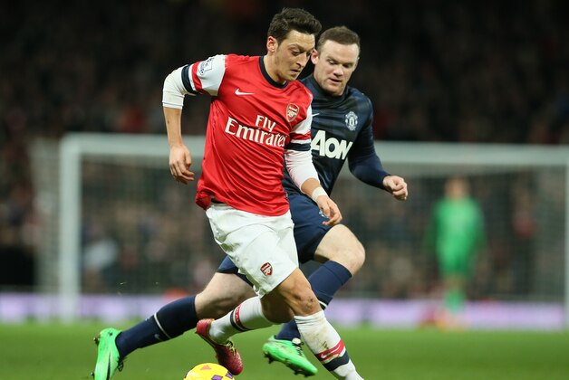 Arsenal's Mesut Ozil, left, shields the ball from Manchester United's Wayne Rooney during their English Premier League soccer match between Arsenal and Manchester United at the Emirates stadium in London, Wednesday, Feb. 12, 2014. (AP Photo/Alastair Grant)