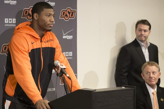 This photo provided by Oklahoma State University Athletics shows Oklahoma State basketball player Marcus Smart, left, addressing the media at a news conference in Stillwater, Okla., Sunday, Feb. 9, 2014, in regard to an altercation during an NCAA college basketball game the day before. Smart was suspended three games by the Big 12 for shoving a fan. Oklahoma State athletic director Mike Holder, bottom right, and Oklahoma State basketball coach Travis Ford look on. (AP Photo/Oklahoma State University Athletics, Bruce Waterfield)