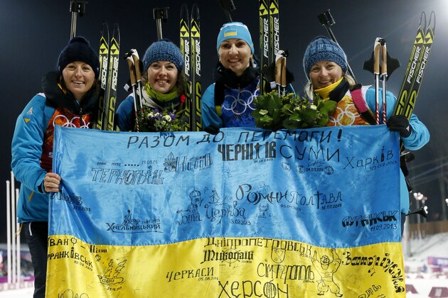 Ukraine's relay team Vita Semerenko, Juliya Dzhyma, Olena Pidhrushna and Valj Semerenko, from left, celebrate with a Ukrainian flag with writings on it after winning the gold during the women's biathlon 4x6k relay, at the 2014 Winter Olympics, Friday, Feb. 21, 2014, in Krasnaya Polyana, Russia. (AP Photo/Dmitry Lovetsky)