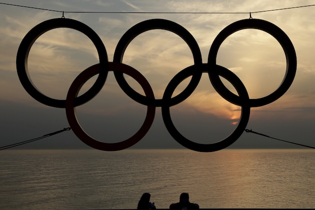 Olympic volunteers stand under a set of Olympic Rings as they watch the sun set over the Black Sea a day after the close of the 2014 Winter Olympics, Monday, Feb. 24, 2014, in Sochi, Russia. (AP Photo/Charlie Riedel)