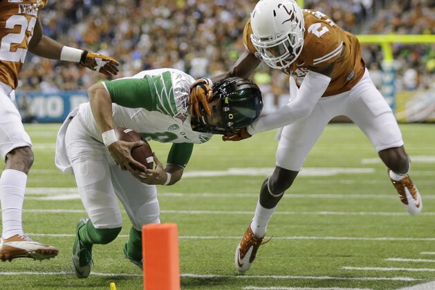 Oregon's Marcus Mariota (8) is pulled down by his helmet by Texas' Mykkele Thompson (2) during the first quarter in the Valero Alamo Bowl NCAA college football game, Monday,  Dec. 30, 2013, in San Antonio. (AP Photo/Eric Gay)