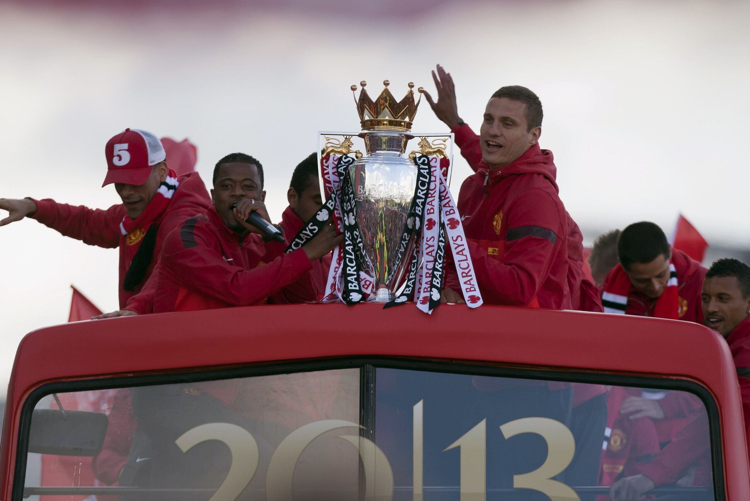 Manchester United's Nemanja Vidic, centre right, and Patrice Evra, centre left, hold the trophy on a bus outside Old Trafford Stadium as the team parade across Manchester after winning the English Premier League, Manchester, England, Monday May 13, 2013. Manager Alex Ferguson will retire at the end of the season after more than 26 years in charge at the club. (AP Photo/Jon Super)
