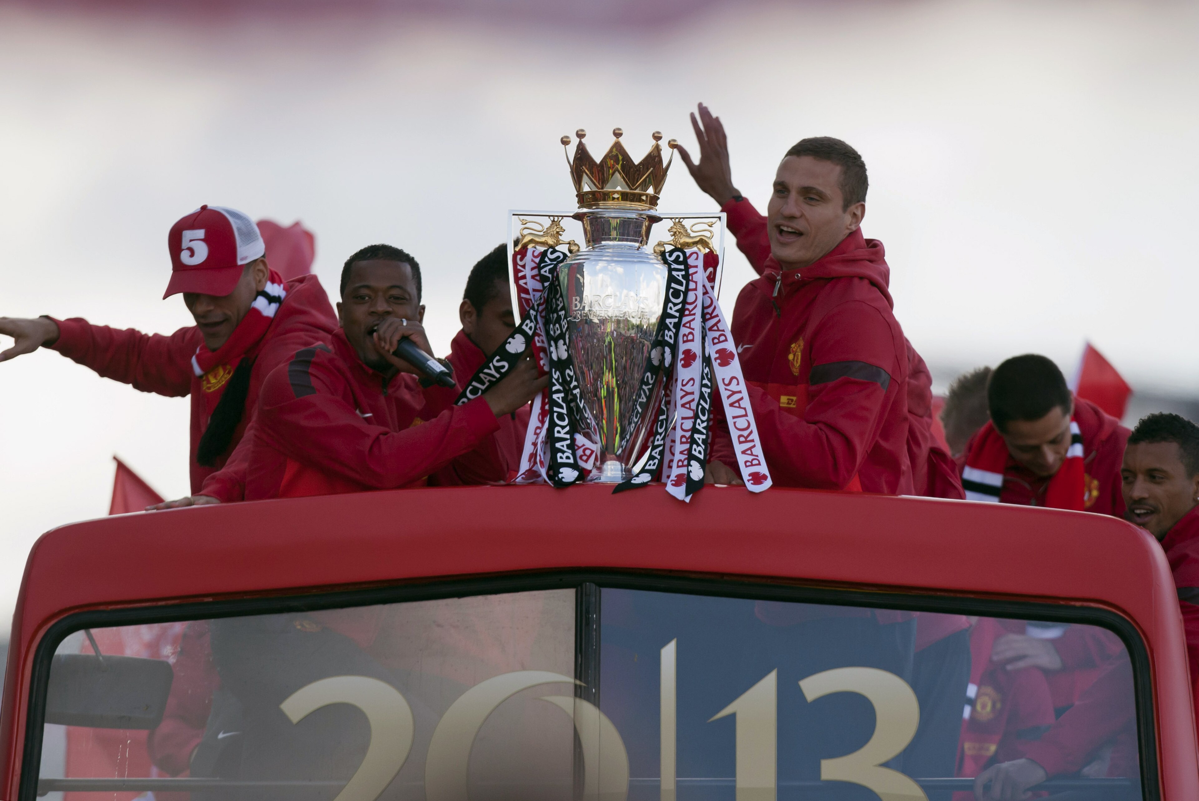 Manchester United's Nemanja Vidic, centre right, and Patrice Evra, centre left, hold the trophy on a bus outside Old Trafford Stadium as the team parade across Manchester after winning the English Premier League, Manchester, England, Monday May 13, 2013. Manager Alex Ferguson will retire at the end of the season after more than 26 years in charge at the club. (AP Photo/Jon Super)