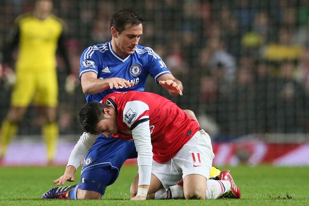 Arsenal's Mesut Ozil, right is lifted off the ball by Chelsea's Frank Lampard after the two clashed during their English Premier League soccer match between Arsenal and Chelsea at the Emirates stadium in London, Monday, Dec. 23, 2013. (AP Photo/Alastair Grant)