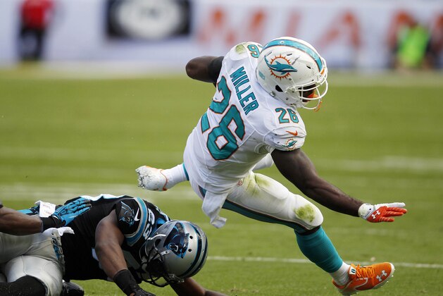 Nov 24, 2013; Miami Gardens, FL, USA; Miami Dolphins running back Lamar Miller (26) runs the ball as Carolina Panthers cornerback Melvin White (23) and strong safety Robert Lester (38) attempt the tackle in the second quarter of a game at Sun Life Stadium. Mandatory Credit: Robert Mayer-USA TODAY Sports