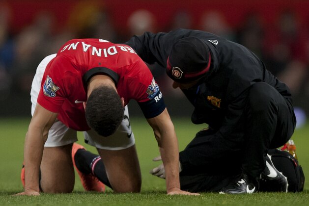 Manchester United's Rio Ferdinand, left, kneels on the pitch before limping off injured during his team's English FA Cup third round soccer match against Swansea City at Old Trafford Stadium, Manchester, England, Sunday Jan. 5, 2014. Manchester United lost 2-1 (AP Photo/Jon Super)
