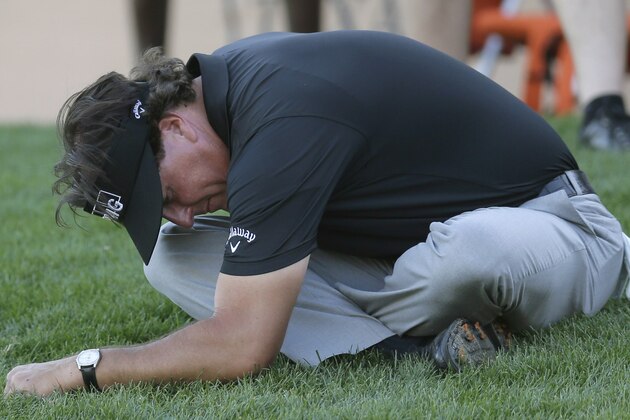 Phil Mickelson stretches on the grass as his playing partners finish the 16th hole during the second round of the Texas Open golf tournament on Friday, March 28, 2014, in San Antonio. (AP Photo/Eric Gay)