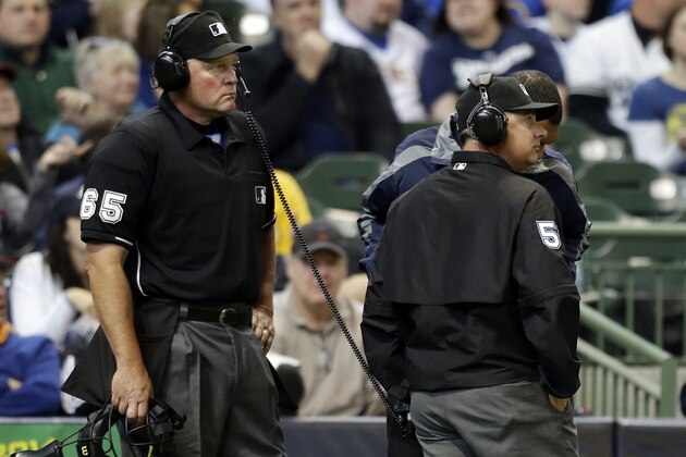 Umpire Ted Barrett (65) listens to the central replay booth in New York in the sixth inning of an opening day baseball game between the Atlanta Braves and Milwaukee Brewers, Monday, March 31, 2014, in Milwaukee. An umpire's call has been overturned for the first time under Major League Baseball's expanded replay system, with Brewers' Ryan Braun ruled out instead of safe. (AP Photo/Jeffrey Phelps)