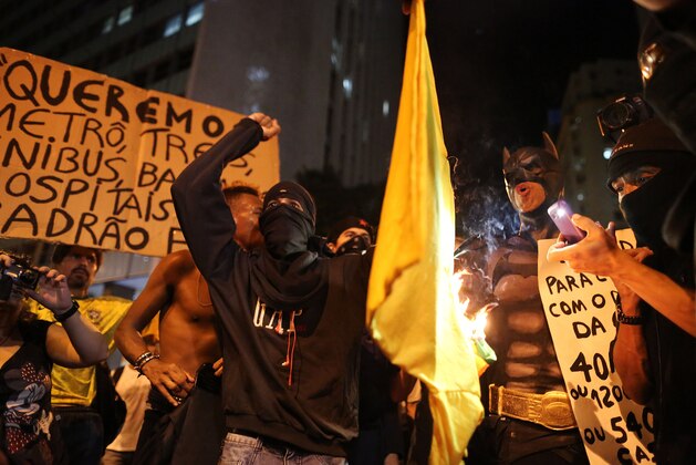 Masked demonstrators set fire to a jersey with the colors of Brazilian national soccer team during protest against the World Cup 2014, in Rio de Janeiro, Brazil, Thursday, March 27, 2014. Demonstrators call for better schools, health care, questioning the billions spent to host this year's World Cup and the 2016 Olympics. (AP Photo/Leo Correa)