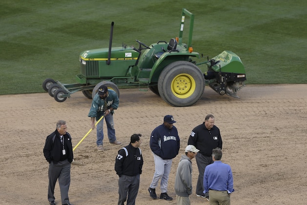 Seattle Mariners manager Lloyd McClendon, bottom center, talks with umpires Jim Reynolds (77) and Fieldin Culbreth (25) as members of the grounds crew work on the infield before a baseball game between the Mariners and the Oakland Athletics was postponed for unplayable field conditions, in Oakland, Calif., Friday, April 4, 2014. (AP Photo/Jeff Chiu)