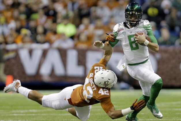 Oregon's Marcus Mariota (8) is pulled down by  Texas' Caleb Bluiett (42) during the first quarter in the Valero Alamo Bowl NCAA college football game, Monday,  Dec. 30, 2013, in San Antonio. (AP Photo/Eric Gay)
