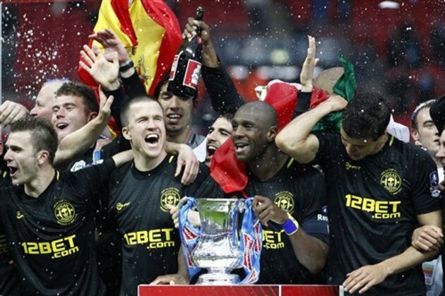 FILE - In this Saturday, May 11, 2013 file photo, Wigan Athletic players including their captain Emmerson Boyce, centre right, celebrate after their 1-0 win over Manchester City in their English FA Cup final soccer match at Wembley Stadium, London. Wigan Athletic hadn’t won a piece of major silverware in its 81-year history until last May, when it pulled off one of the great FA Cup upsets by beating big-spending Manchester City in the final. Now, despite dropping out of the Premier League at the end of last season, it is on course to retain the famous trophy against all the odds. (AP Photo/Jon Super, File)
