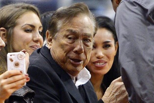 In this photo taken on Friday, Oct. 25, 2013, Los Angeles Clippers owner Donald Sterling, center, and V. Stiviano, right, watch the Clippers play the Sacramento Kings during the first half of an NBA basketball game, in Los Angeles. The NBA is investigating a report of an audio recording in which a man purported to be Sterling makes racist remarks while speaking to Stiviano.  NBA spokesman Mike Bass said in a statement Saturday, April 26, 2014, that the league is in the process of authenticating the validity of the recording posted on TMZ's website. Bass called the comments