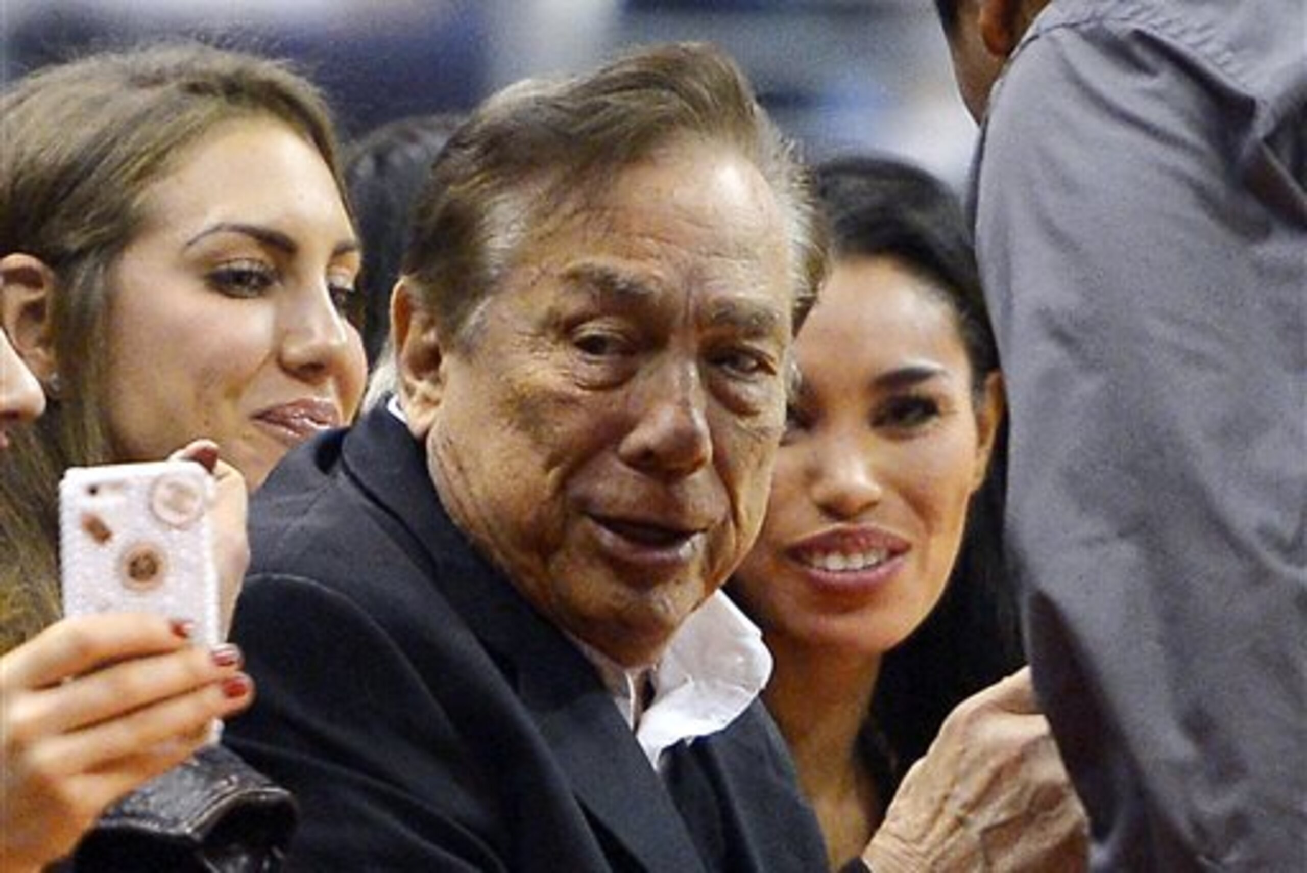 In this photo taken on Friday, Oct. 25, 2013, Los Angeles Clippers owner Donald Sterling, center, and V. Stiviano, right, watch the Clippers play the Sacramento Kings during the first half of an NBA basketball game, in Los Angeles. The NBA is investigating a report of an audio recording in which a man purported to be Sterling makes racist remarks while speaking to Stiviano.  NBA spokesman Mike Bass said in a statement Saturday, April 26, 2014, that the league is in the process of authenticating the validity of the recording posted on TMZ's website. Bass called the comments