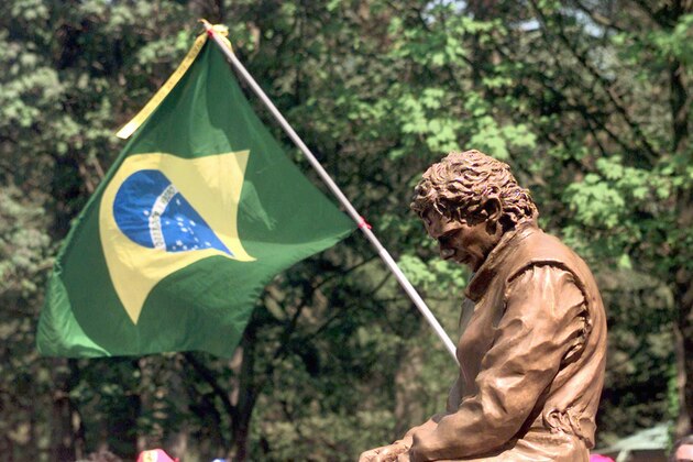 A fan waves a Brazilian flag behind the statue of the late Brazilian Formula One driver Ayrton Senna, Friday, April 25, 1997, during the unveiling ceremony at the Tamburello turn of the Imola autodrome, the site of the fatal crash of the three-time World Champion who died on this circuit on May 1, 1994. (AP Photo/Luca Bruno)