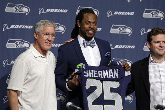 Seattle Seahawks' Richard Sherman, center, holds up a jersey before a news conference as he poses with head coach Pete Carroll, left, and general manager John Schneider Wednesday, May 7, 2014, at the team's headquarters in Renton, Wash. Sherman signed a four-year contract extension Wednesday with the Seahawks, a deal that makes him one of the highest-paid cornerbacks in NFL history. (AP Photo/Elaine Thompson)