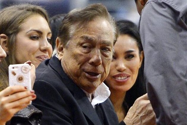 In this photo taken on Friday, Oct. 25, 2013, Los Angeles Clippers owner Donald Sterling, center, and V. Stiviano, right, watch the Clippers play the Sacramento Kings during the first half of an NBA basketball game, in Los Angeles. The NBA is investigating a report of an audio recording in which a man purported to be Sterling makes racist remarks while speaking to Stiviano.  NBA spokesman Mike Bass said in a statement Saturday, April 26, 2014, that the league is in the process of authenticating the validity of the recording posted on TMZ's website. Bass called the comments