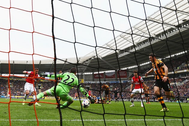 HULL, ENGLAND - APRIL 20:  Lukas Podolski (L) of Arsenal shoots past Steve Harper the Hull City goalkeeper and James Chester (R) of Hull City to score his sides third goal during the Barclays Premier League match between Hull City and Arsenal at KC Stadium on April 20, 2014 in Hull, England.  (Photo by Matthew Lewis/Getty Images)