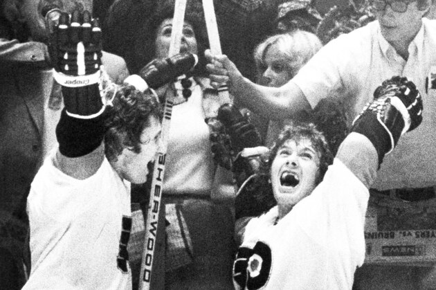 Philadelphia Flyers teammates Don Saleski, left, and Bobby Clarke celebrate as the buzzer sounded to signal to Flyers Stanley Cup victory over the Boston Bruins in afternoon, Sunday, May 20, 1974 in Philadelphia. As Clarke pays attention to the scoreboard, a fan reaches in to take Clarke stick as a souvenir. (AP Photo)