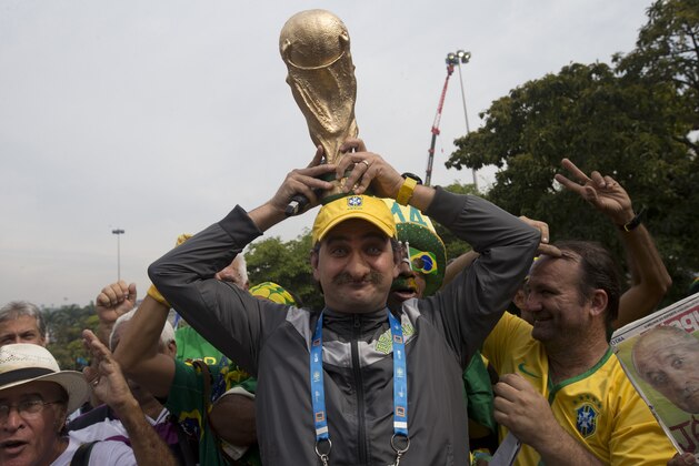 A Brazil soccer fan in the likeness of coach Luiz Felipe Scolari, wearing a fake nose, holds a replica of the FIFA World Cup trophy as he poses for photos with fans outside the venue where Brazil's coach announced his squad for the upcoming international soccer tournament in Rio de Janeiro, Brazil, Wednesday, May 7, 2014. The team will mix talented young stars such as Neymar and Oscar with more experienced players such as Dani Alves, David Luiz, Thiago Silva and Hulk. Past stars such as Ronaldinho, Kaka and Robinho were left off the squad as expected. (AP Photo/Silvia Izquierdo)