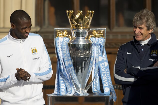 Manchester City's Yaya Toure, left, and manager Manuel Pellegrini stand by the trophy as the team celebrate in the city centre the day after they won the English Premier League title, Manchester, England, Monday May 12, 2014. (AP Photo/Jon Super)