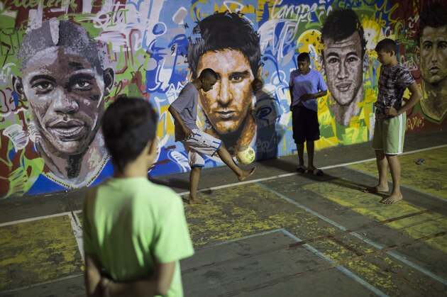 Boys practice freestyle soccer next to a mural depicting soccer players, from left; Italy's Mario Balotelli, Argentina's Lionel Messi, Brazil's Neymar and Portugal's Cristiano Ronaldo, at a slum in Rio de Janeiro, Brazil, Thursday, June 5, 2014. The Word Cup soccer tournament is set to begin in just a few days, with Brazil and Croatia playing in the opening match on June 12.  (AP Photo/Felipe Dana)