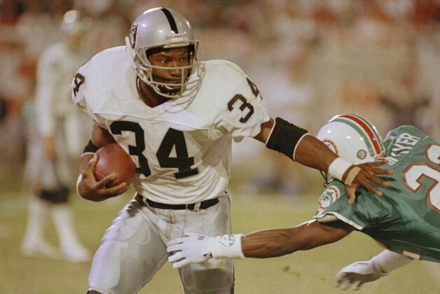 Los Angeles Raiders running back Bo Jackson (34) pushes away Miami Dolphins corner back Tim McKyer (22) during the third quarter of game in Miami's Joe Robbie stadium, Nov. 20, 1990. (AP Photo/Beth Keiser)