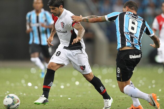 Ever Banega of Argentina's Newell's Old Boys, left, fights for the ball with Edinho of Brazil's Gremio during their Copa Libertadores soccer match in Porto Alegre, Brazil, Thursday, March 13, 2014. (AP Photo/Nabor Goulart)
