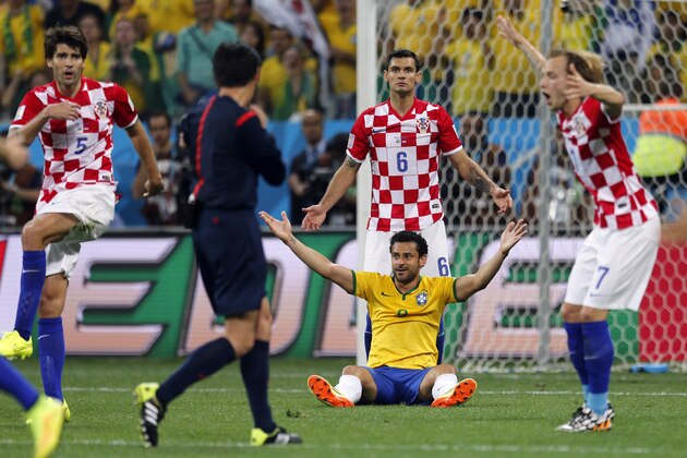 Brazil's Fred sits on the pitch as Croatian players Vedran Corluka (5), Dejan Lovren (6) and Ivan Rakitic (7) protest after referee Yuichi Nishimura, from Japan, called a penalty against Croatia during the group A World Cup soccer match in the opening game of the tournament at Itaquerao Stadium in Sao Paulo, Brazil, Thursday, June 12, 2014. Brazil's Neymar scored on a penalty kick after the play. (AP Photo/Frank Augstein)