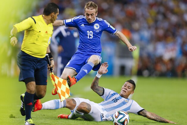 Bosnia's Edin Visca (19) leaps over Argentina's Marcos Rojo (16) as he chases the ball during the group F World Cup soccer match between Argentina and Bosnia at the Maracana Stadium in Rio de Janeiro, Brazil, Sunday, June 15, 2014.  (AP Photo/Kirsty Wigglesworth)