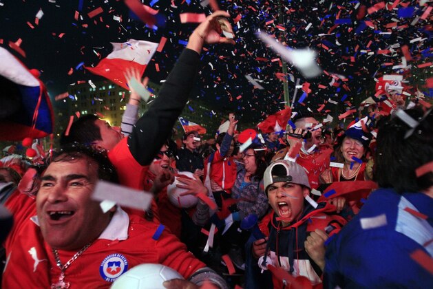 In this Friday, June 13, 2014 photo, soccer fans cheer as they watch Chile's Alexis Sanchez score the first goal of the World Cup match between Chile and Australia, via a live broadcast on a giant screen in front of La Moneda presidential palace, in Santiago, Chile. Sanchez produced a dynamic performance to lead Chile to a 3-1 win over Australia at the Arena Pantanal in Cuiaba, Brazil. (AP Photo/Luis Hidalgo)