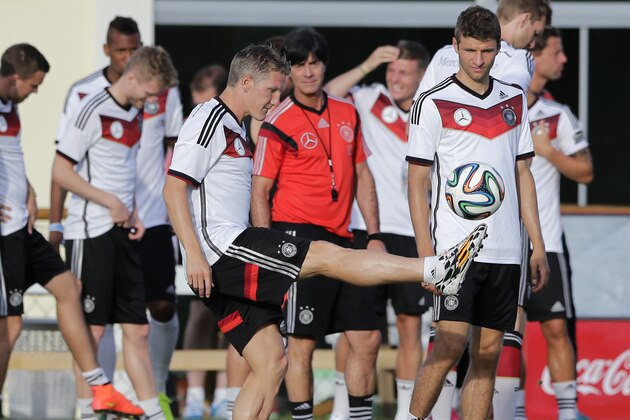 Germany's national soccer player Bastian Schweinsteiger joggles a ball in front of head coach Joachim Loew, background center, and teammate Thomas Mueller, right, during a training session in Santo Andre near Porto Seguro, Brazil, Wednesday, June 18, 2014. Germany play in group G of the 2014 soccer World Cup. (AP Photo/Matthias Schrader)