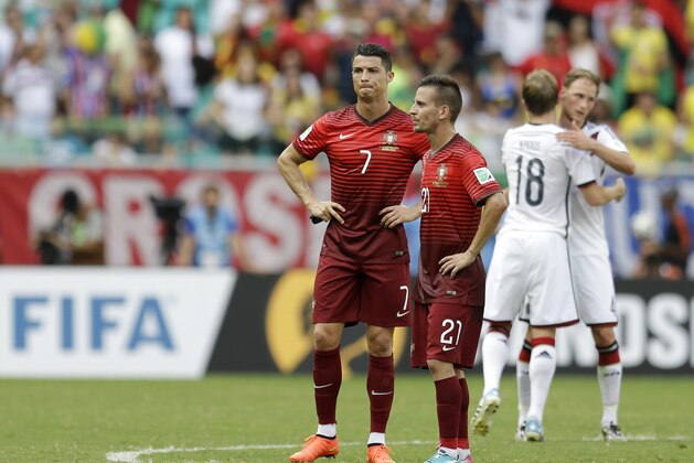 Portugal's Cristiano Ronaldo (7) stands with his teammate Joao Pereira (21) while German players celebrate following their 4-0 victory over Portugal during the group G World Cup soccer match between Germany and Portugal at the Arena Fonte Nova in Salvador, Brazil, Monday, June 16, 2014.  (AP Photo/Natacha Pisarenko)