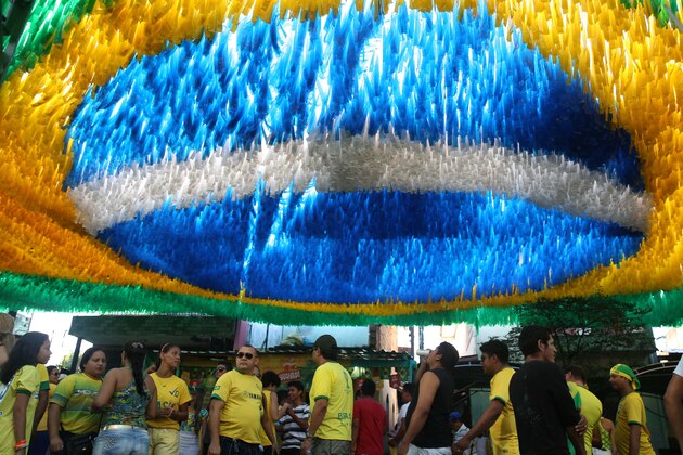 Soccer fans walk below a street decoration of the Brazilian flag, during the Brazil soccer World Cup match against Cameroon, in Manaus, Brazil, Monday, June 23, 2014. Brazil's Neymar scored twice in the first half to lead Brazil to a 4-1 win over Cameroon on Monday, helping the hosts secure a spot in the second round of the soccer World Cup. (AP Photo/Martin Mejia)