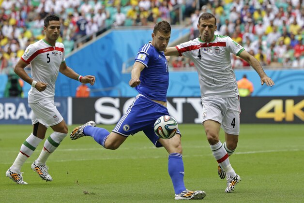 Bosnia's Edin Dzeko, center, gets in a shot despite the challenge of Iran's Jalal Hosseini, right, during the group F World Cup soccer match between Bosnia and Iran at the Arena Fonte Nova in Salvador, Brazil, Wednesday, June 25, 2014. (AP Photo/Sergei Grits)