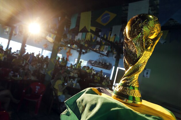Brazilian residents watch the opening match of FIFA World Cup between Brazil and Croatia behind a replica of the trophy in Porto Seguro, Brazil, Thursday, June 12, 2014. (AP Photo/Matthias Schrader)