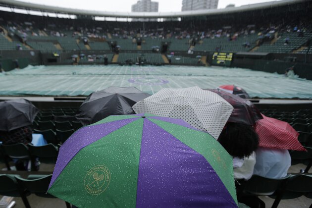 Spectators sit under umbrellas as rain falls and play is suspended on No 1 Court in the match between Grigor Dimitrov of Bulgaria and Leonardo Mayer of Argentina at the All England Lawn Tennis Championships in Wimbledon, London, Monday, June 30, 2014. (AP Photo/Ben Curtis)
