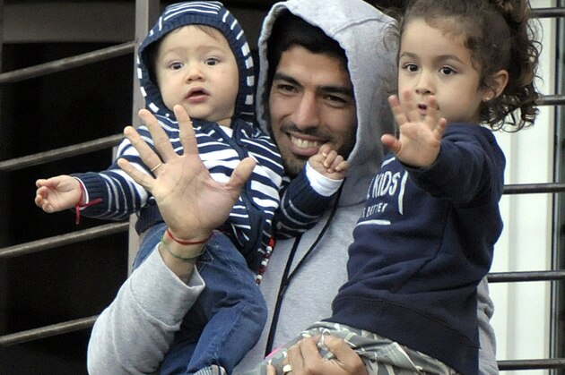 Uruguay's soccer player Luis Suarez holds his children as he greets fans from their home's balcony on the outskirts of Montevideo, Uruguay, Friday, June 27, 2014. Suarez returned to Montevideo early Friday, arriving too late to see the hundreds of Uruguay fans who had gathered the previous night to give him a hero's welcome despite his World Cup banishment. (AP Photo/Matilde Campodonico)