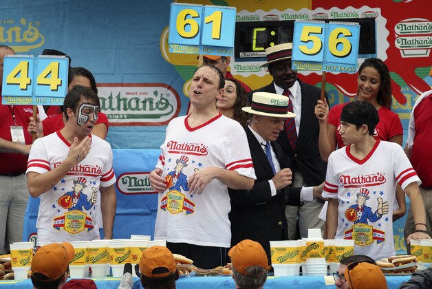 Joey Chestnut, center, reacts alongside Tim Janus, left, and Matt Stonie, right, after competing in the Nathan's Famous Fourth of July International Hot Dog Eating contest at Coney Island, Friday, July 4, 2014, in New York. Chestnut won his eighth contest by finishing 61 hotdogs and buns. (AP Photo/John Minchillo)