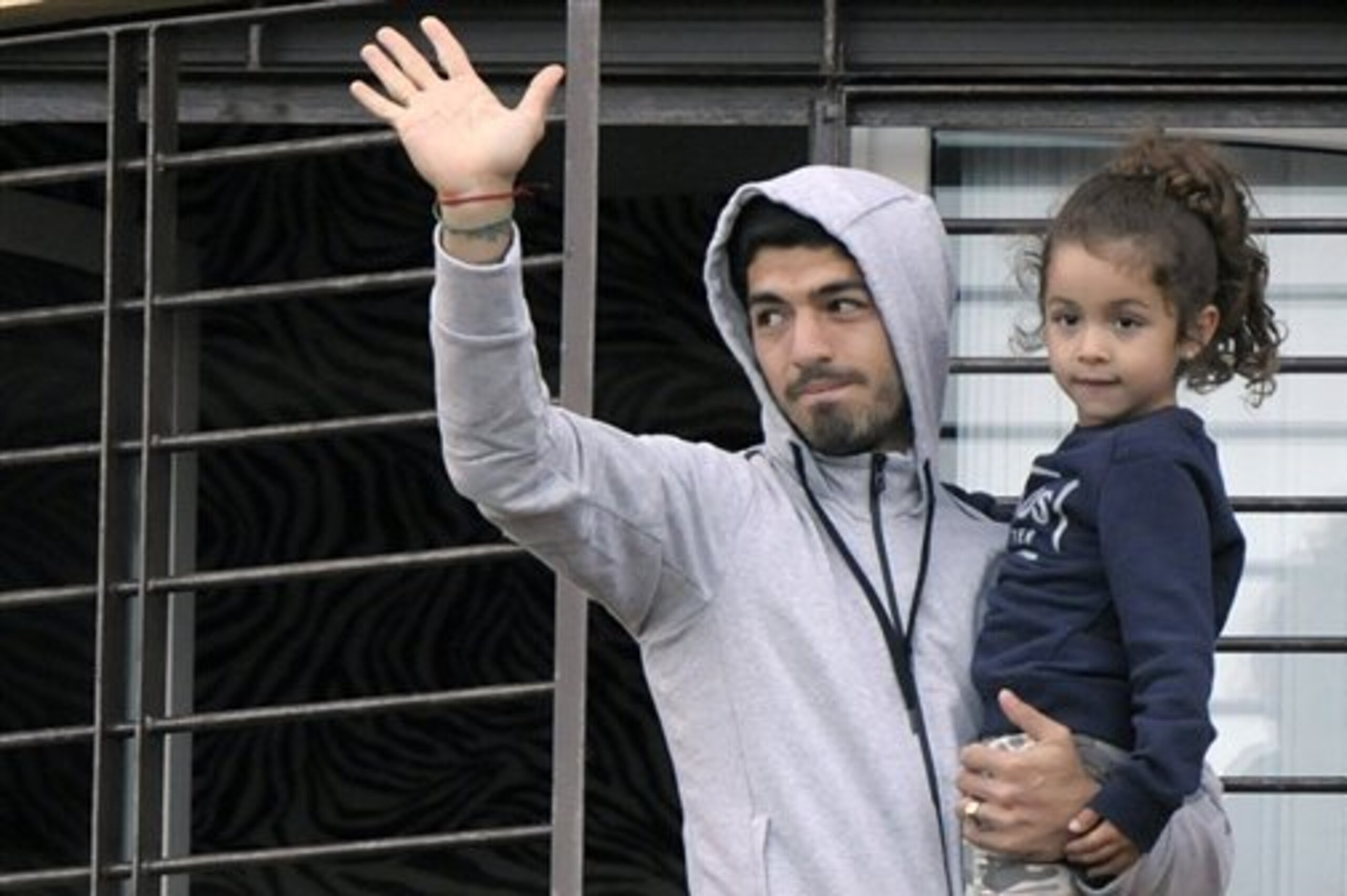 Uruguay's soccer player Luis Suarez holds his daughter as he greets fans from their home's balcony on the outskirts of Montevideo, Uruguay, Friday, June 27, 2014. Suarez returned to Montevideo early Friday, arriving too late to see the hundreds of Uruguay fans who had gathered the previous night to give him a hero's welcome despite his World Cup banishment. (AP Photo/Matilde Campodonico)