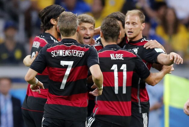 Brazil's Oscar, right, passes by celebrating German players after Germany's Thomas Mueller scored the opening goal during the World Cup semifinal soccer match between Brazil and Germany at the Mineirao Stadium in Belo Horizonte, Brazil, Tuesday, July 8, 2014. (AP Photo/Frank Augstein)