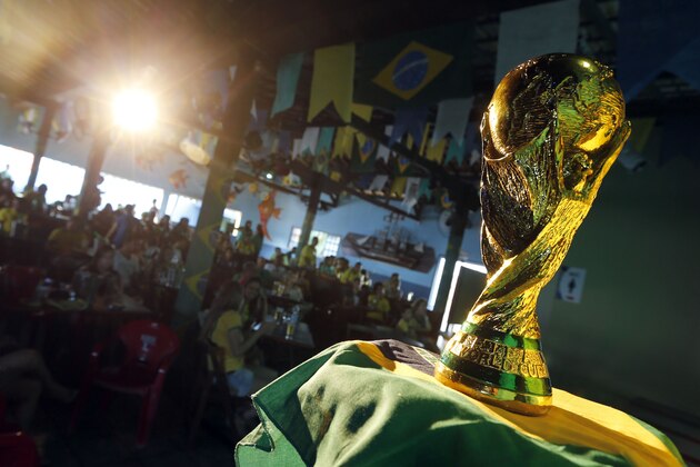 Brazilian residents watch the opening match of FIFA World Cup between Brazil and Croatia behind a replica of the trophy in Porto Seguro, Brazil, Thursday, June 12, 2014. (AP Photo/Matthias Schrader)