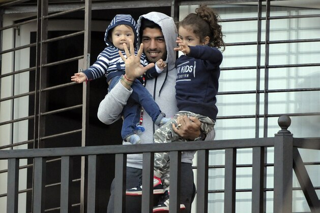 Uruguay's soccer player Luis Suarez holds his children as he greets fans from their home's balcony on the outskirts of Montevideo, Uruguay, Friday, June 27, 2014. Suarez returned to Montevideo early Friday, arriving too late to see the hundreds of Uruguay fans who had gathered the previous night to give him a hero's welcome despite his World Cup banishment. (AP Photo/Matilde Campodonico)