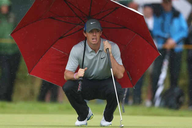 Rory McIlroy of Northern Ireland kneels under an umbrella as he waits to play on the 4th green during the third day of the British Open Golf championship at the Royal Liverpool golf club, Hoylake, England, Saturday July 19, 2014. (AP Photo/Jon Super)