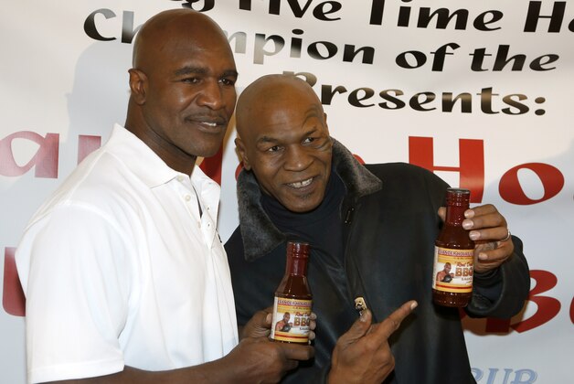 Former heavyweight champions Mike Tyson, right, and Evander Holyfield during a promotional event for Holyfield's Real Deal barbecue sauce at a Chicago grocery store Saturday, Feb. 16, 2013. (AP Photo/Charlie Arbogast)