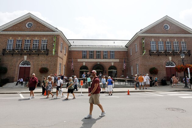Fans walk outside the Baseball Hall of Fame and Museum on Friday, July 25, 2014, in Cooperstown, N.Y. Former Major League Baseball managers Joe Torre, Bobby Cox and Tony La Russa, with pitchers Greg Maddux and Tom Glavine and slugger Frank Thomas, will be inducted to the hall on Sunday. (AP Photo)