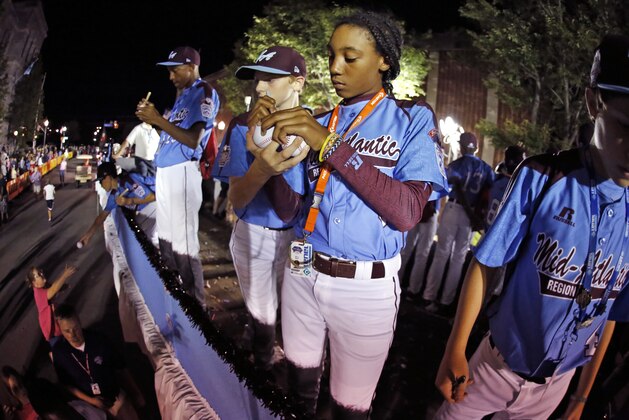 A teammate on the Taney Little League team from Philadelphia, helps hold baseballs for Mo'ne Davis, center, to sign as the team rides in the Little League Grand Slam Parade as it makes its way through downtown Williamsport, Pa., Wednesday, Aug. 13, 2014. The Little League World Series tournament begins Thursday, August 14, in South Williamsport, Pa.. Davis is one of two girls competing in the Little League World Series tournament this year.  (AP Photo/Gene J. Puskar)